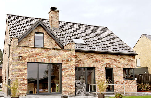 A modern brick house with a gray tiled roof, large glass doors, and a chimney