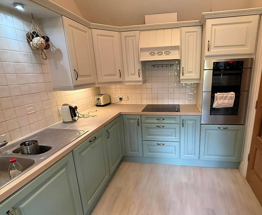 Compact kitchen with pale green and cream cabinets, a built-in oven, electric stove, and tiled backsplash