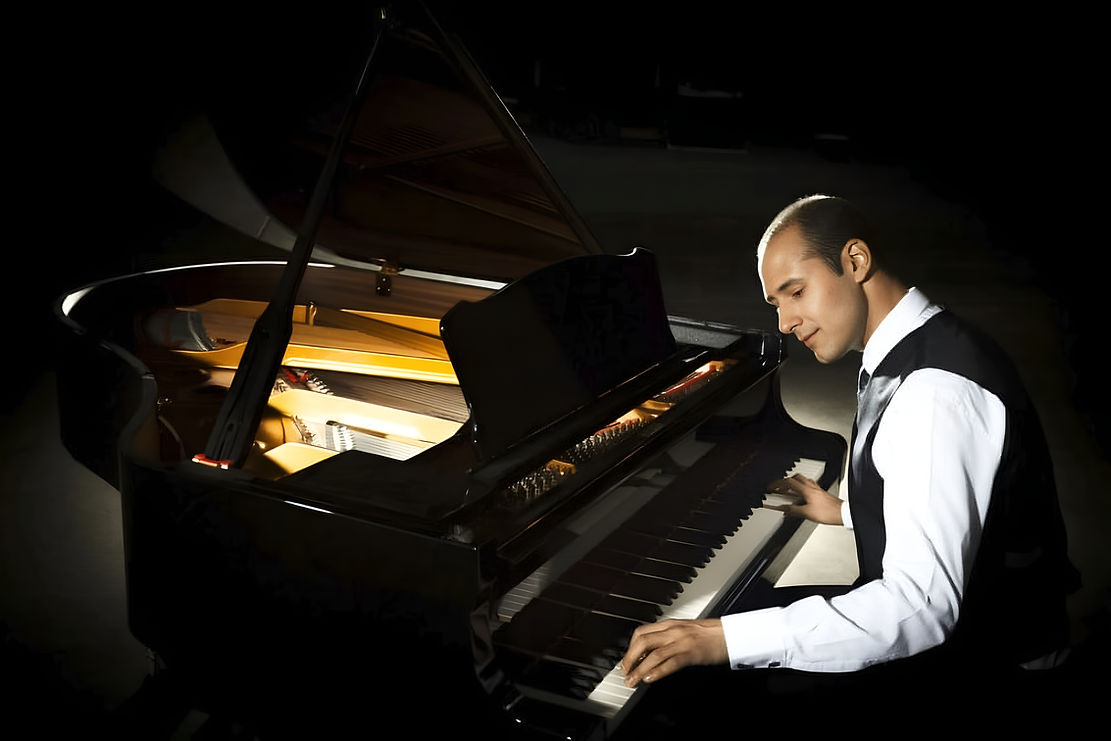 A man in a white shirt and black vest plays a grand piano