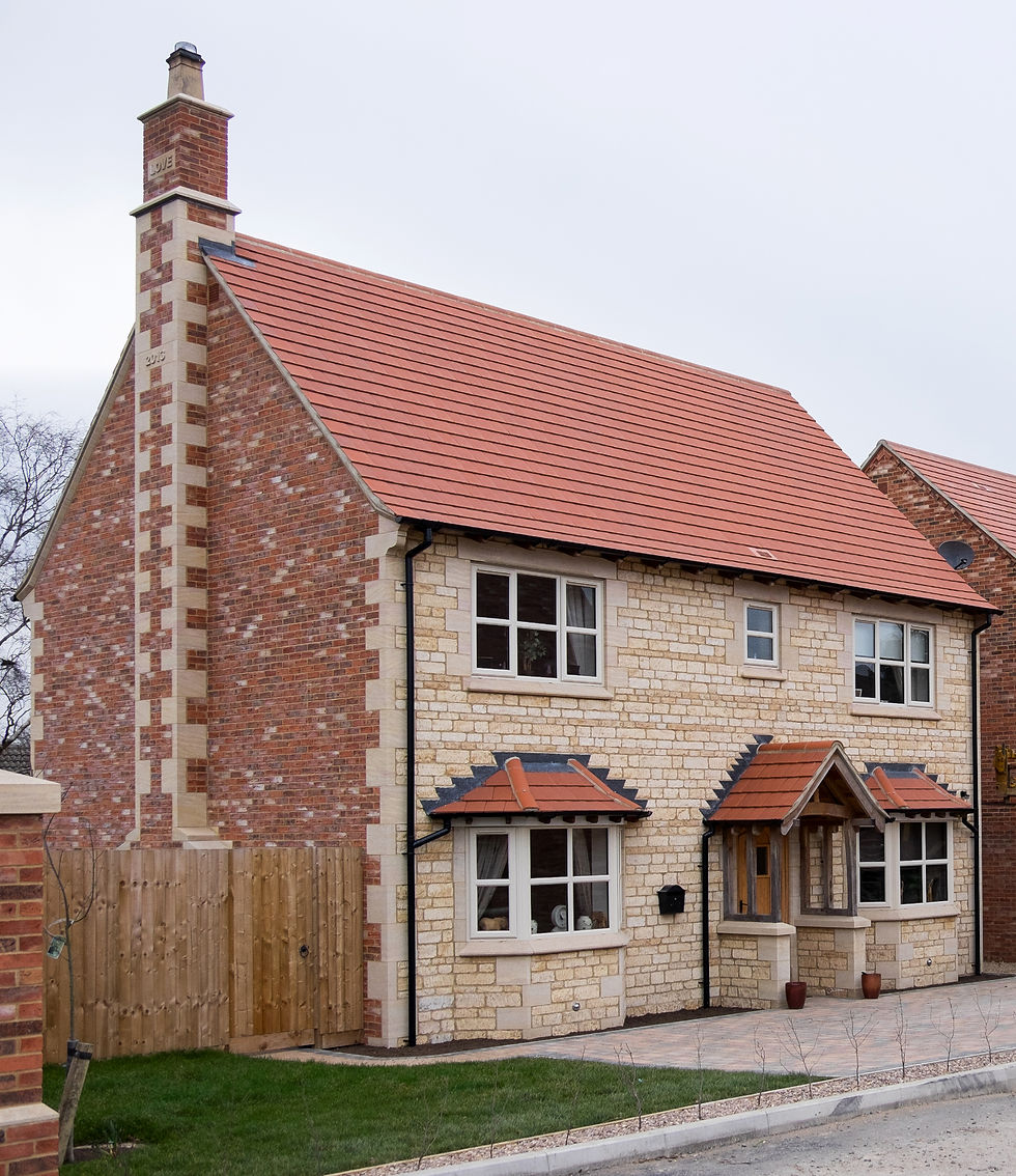 Newly constructed brick and stone house with a red tiled roof and a yellow telehandler on site.