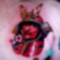 Vivid tattoo of a red samurai warrior with ornate helmet and cherry blossom.