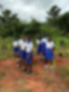 Students in uniforms stand together, surrounded by trees and bushes outdoors Projects Abroad.