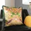 Thumbnail: Mustard tropical print cushion with colourful floral design and green fringe trim, styled on a dark chair.