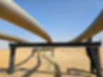 Steel pipelines stretch across a sandy desert under a clear blue sky. Stainless steel piping resting on carbon steel pipe support with no barrier between the pipe and the support causing galvanic corrosion and erosion.