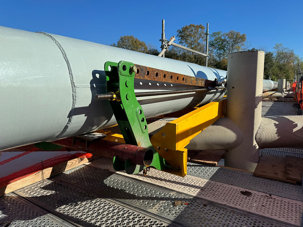 Large industrial pipeline with green and yellow bracket on a platform. Bright blue sky and trees in the background.