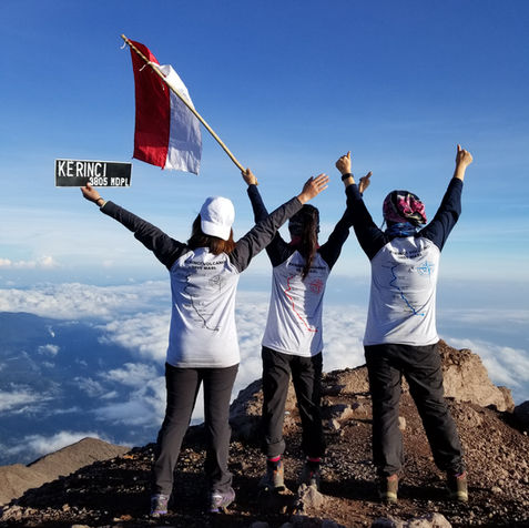 Three hikers celebrate atop Mount Kerinci, holding Indonesian flag