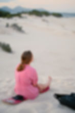 A girl in a pink shirt sits on a sand board on the dunes of Florianopolis