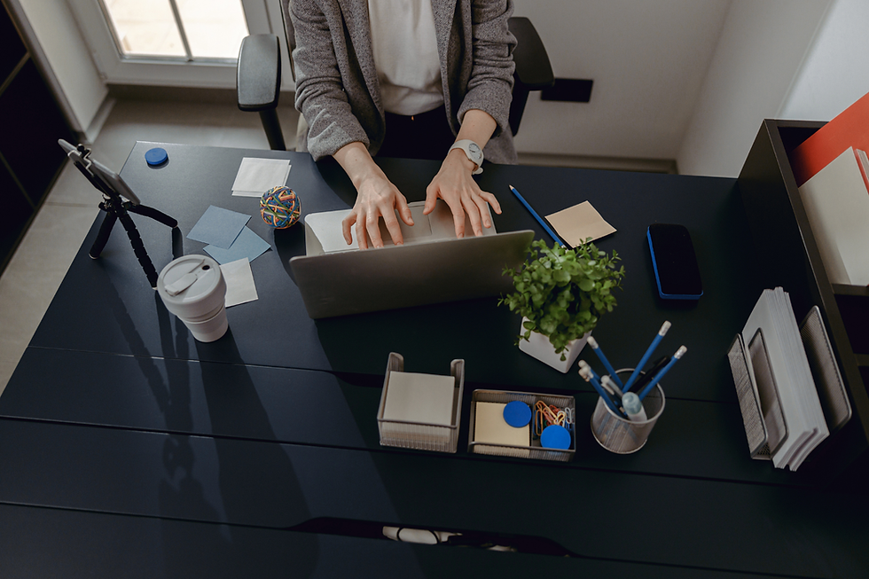 Person typing on a laptop at a tidy desk with plants, notebooks, and a camera on a tripod. Neutral tones and organized workspace.