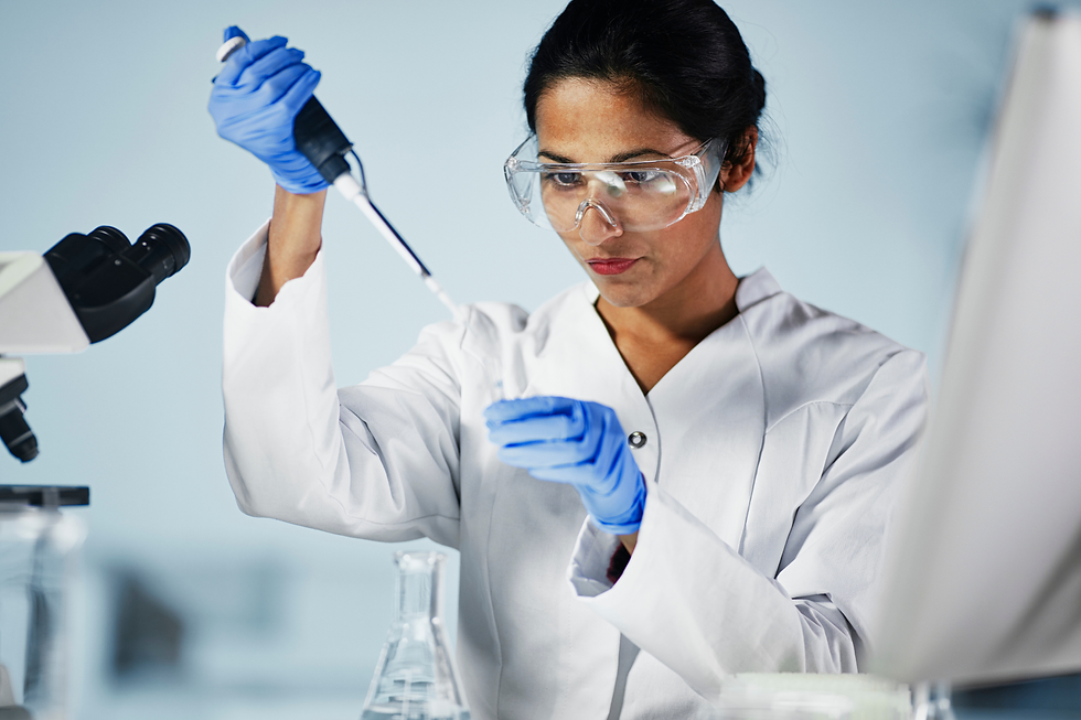 Female scientist in lab coat, goggles and blue gloves uses a pipette beside a microscope, focused in a bright lab.