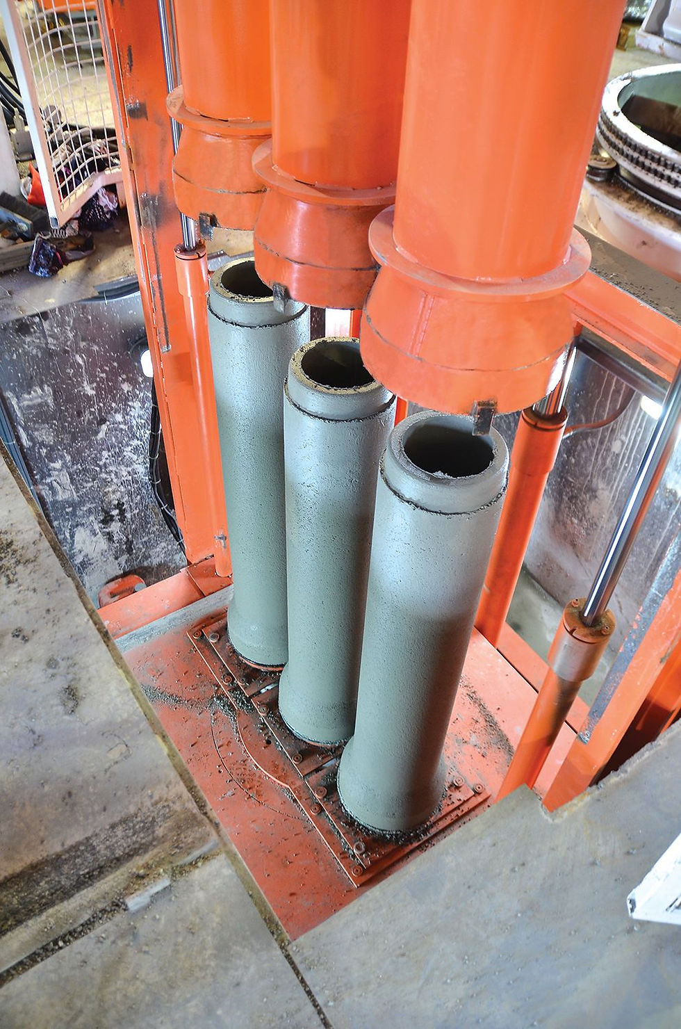 ndustrial Concrete Pipe Machine showing three concrete pipes being formed simultaneously with hydraulic forming heads and vertical moulds.