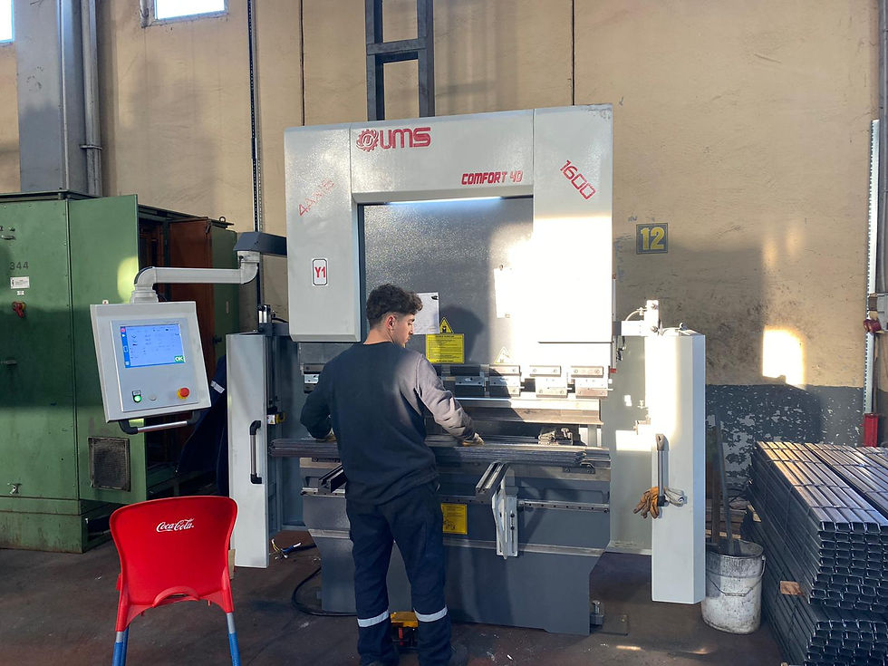 Atölyede UMS COMFORT 40 pres makinesini kullanan işçi; sol tarafında makine kontrol paneli, sağ arka planda bükümlü hazır metal parçalar.