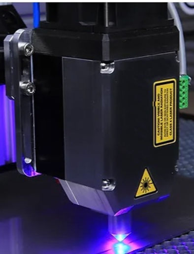 Lazer Kesim Kafası: Metal yüzey üzerinde yüksek hassasiyetle hareket eden kesim ünitesi.
İşlem Anı: Lazer ışınının metal sac ile temas ettiği noktada oluşan parlak mavi/mor ışık, kesim işleminin aktif olduğunu gösterir.
Güvenlik Uyarıları: Kesim kafasının üzerinde sarı renkli "Lazer Radyasyonu" ve güvenlik sınıfını belirten standart uyarı etiketleri yer almaktadır.
Teknoloji: Bu görsel, malzemenin temassız, hızlı ve pürüzsüz bir şekilde işlendiği modern fiber lazer teknolojisini temsil eder.