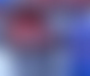 The image shows a massive, orange-colored, heavy-duty steel industrial concrete pipe profile inside a high-ceilinged factory. This mold features a cylindrical body, an octagonal metal plate at the top, and numerous metal clamp systems that secure the parts.