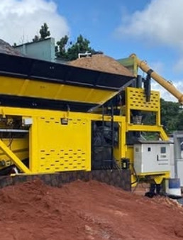 shows a yellow mobile concrete batching plant machine filled with sand, a control panel, and a soil pile under cloudy skies.