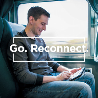 A man on a train types on a tablet. The words Go, Reconnect.
