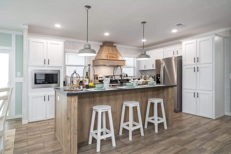 Sample manufactured home kitchen with island, white cabinets, and vinyl plank flooring – shown for illustrative purposes by Oxford Housing Inc. in Alabama.