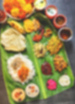 On a banana leaf, rice is in a small pile, surrounded by several curries and bowls of yoghurt and sauces.