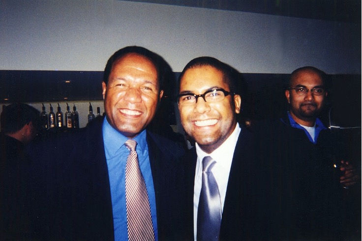 Image of author as a young adult smiling and standing next to his father, also smiling. They are both wearing suits.