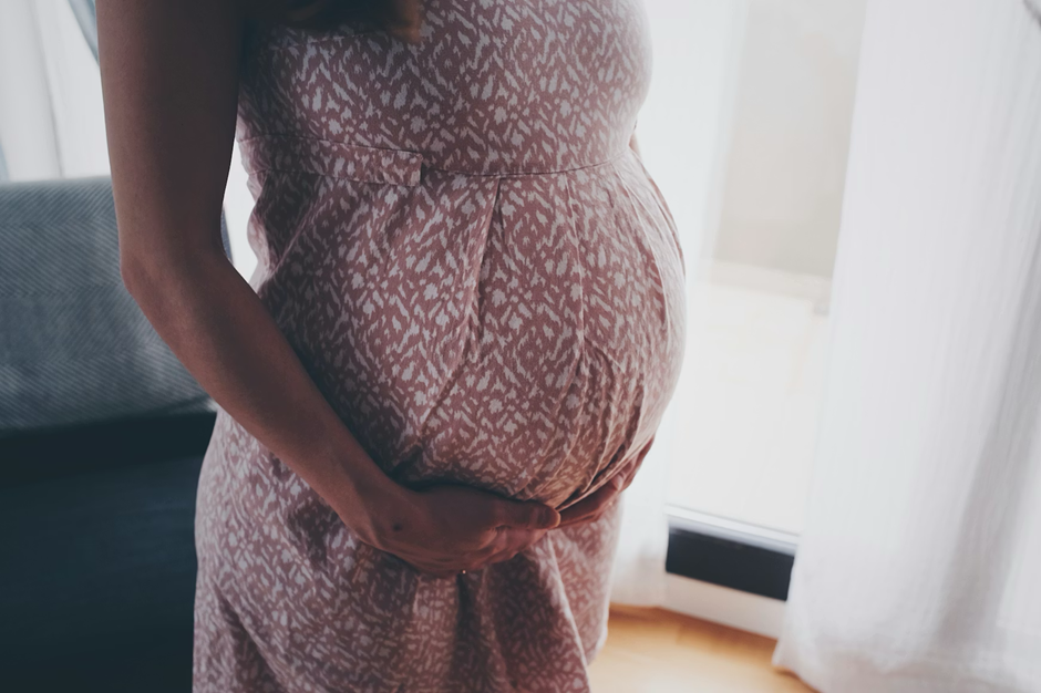 A woman wearing a dress is holding her baby bump with one hand.