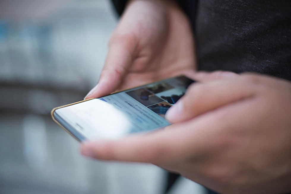 Close-up image of two hands holding a phone displaying a social media page.