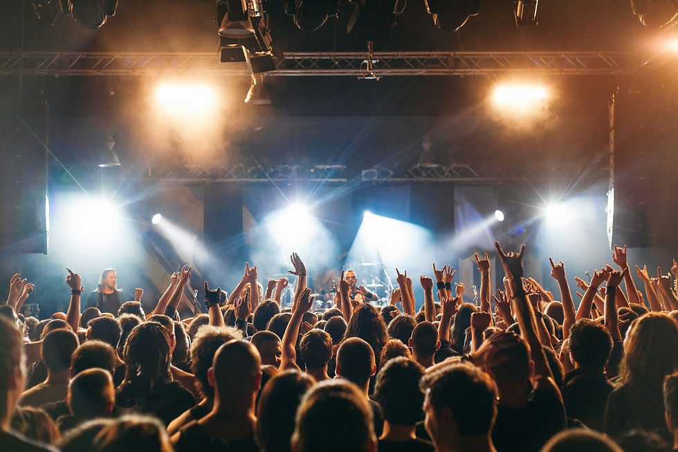 Crowded indoor concert with raised hands, bright stage lights, and musicians onstage, creating an energetic, smoky atmosphere