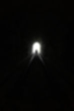 A grayscale image of a man walking towards the end of a dark tunnel towards the light.