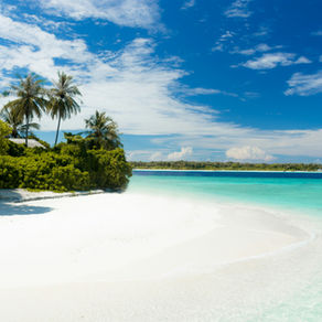 Tropical beach with white sand, turquoise water, palm trees, and a bright blue sky with scattered clouds, calm and sunny