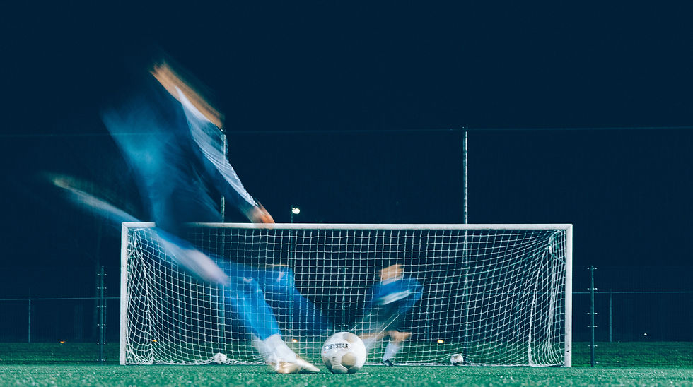 Blurred soccer players in blue sprint past a goal at night, with a ball in front.