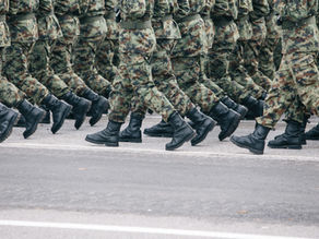 Men in brown and green camouflage uniforms are walking side by side in a parade. The image