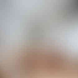 Woman in a modern kitchen sits on a stool at a wooden island, reading. A black dog sits nearby. Bright space with plants and pendant lights.