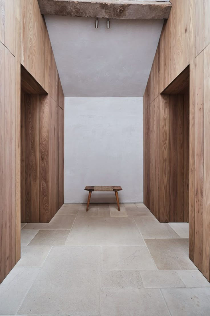Minimalist hallway with wooden walls and stone floor, featuring a small wooden bench against a plain white wall. Simple and serene mood.