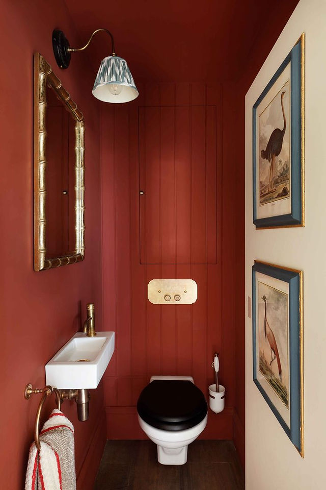 Elegant pink bathroom with a round mirror, white pedestal sink, brass fixtures, and checkered floor. A towel hangs on the sink.