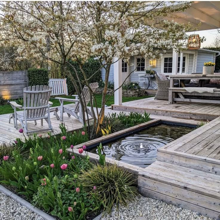 Peaceful garden with wooden deck, chairs, pink tulips, and a small pond with ripples. A cozy house in the background. Spring atmosphere.