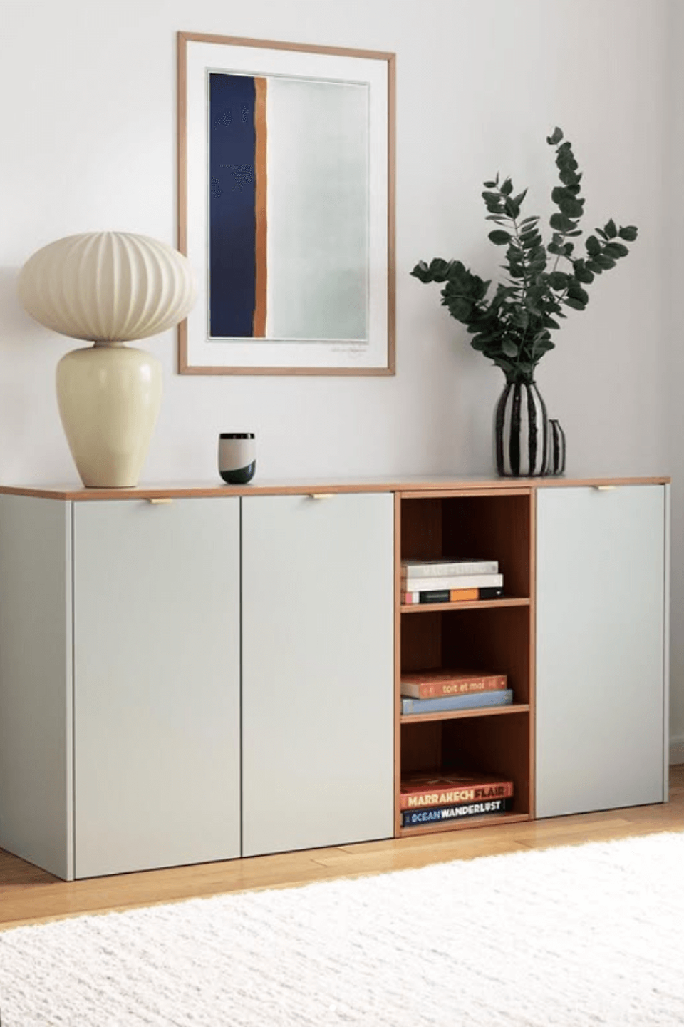 IKEA HACK Minimalist room with a gray cabinet, vase with leaves, lamp, and books. Abstract framed art on the wall; light and airy mood.