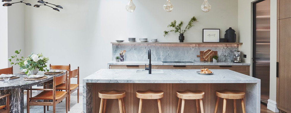 large kitchen island with calacatta marble and black stools, wooden cabinets and a range cooker in a contemporary kitchen extension