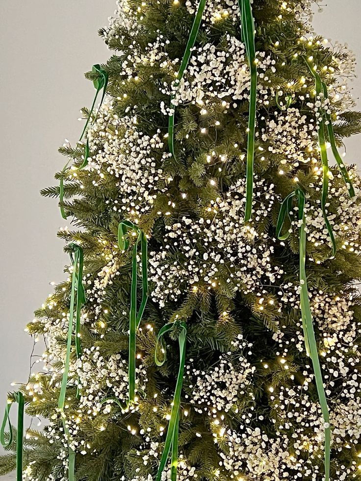 Christmas tree adorned with white flowers, green ribbons, and warm lights in a cozy setting, creating a festive atmosphere.