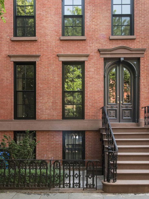 Brownstone building facade with black door, steps, and ornate trim. Fall foliage in front. Calm urban setting, light gray sky.