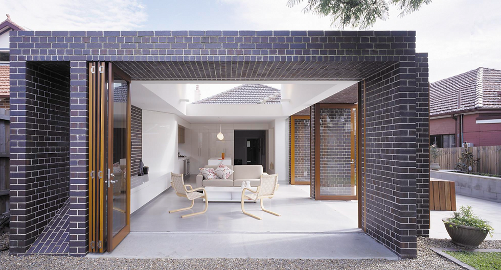 Modern open-plan living room with large glass doors, black brick walls, and a white ceiling. Natural light creates a relaxed atmosphere.