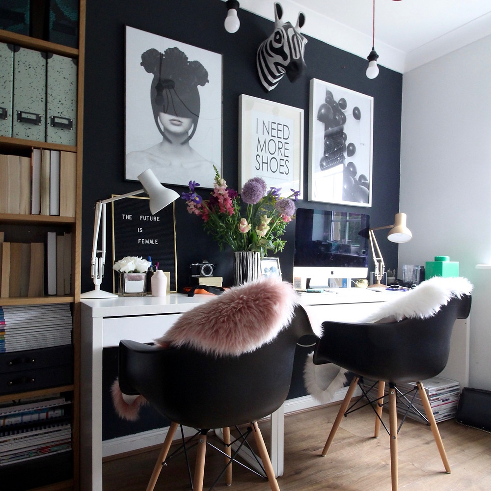 A FASHION INSPIRED HOME OFFICE with white IKEA desks and EAMES black chairs in front of a black wall with fashion posters