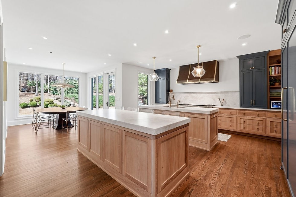 Spacious kitchen with wooden cabinets, marble countertops, and pendant lights. Large windows overlook a garden. Bright, airy atmosphere.