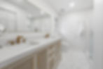 Modern bathroom with white walls and a marble floor. Features a double vanity with gold faucets, a large mirror, and a glass shower.