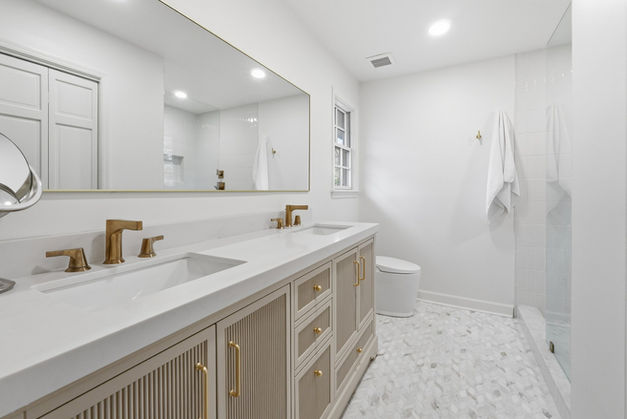 Renovated primary bathroom with oak colored cabinets, white countertops and gold fixtures with glass shower