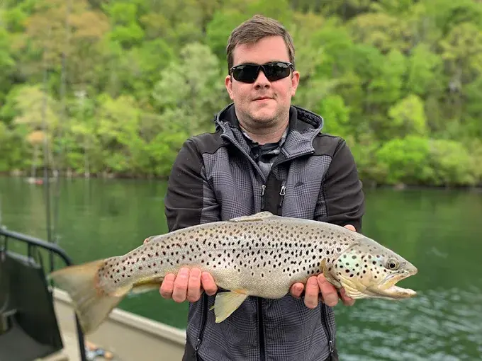 a man holds a trout caught on Lake Taneycomo during a Branson fishing trip with CastAway Charters