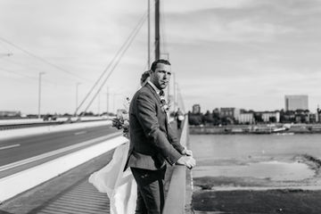 Entspannter Augenblick in Düsseldorf: Der Bräutigam steht auf einer Brücke und genießt genussvoll eine Zigarette. Die Kulisse der Stadt Düsseldorf bildet den Hintergrund für diesen ruhigen Moment. Inmitten der Hochzeitsfeierlichkeiten nimmt sich der Bräutigam einen Augenblick für sich, um die Atmosphäre und die Bedeutung dieses besonderen Tages zu reflektieren.