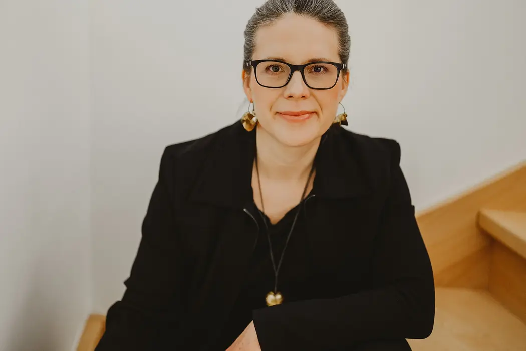 Businessportrait einer Frau in schwarzem Blazer auf einer Holztreppe sitzend.