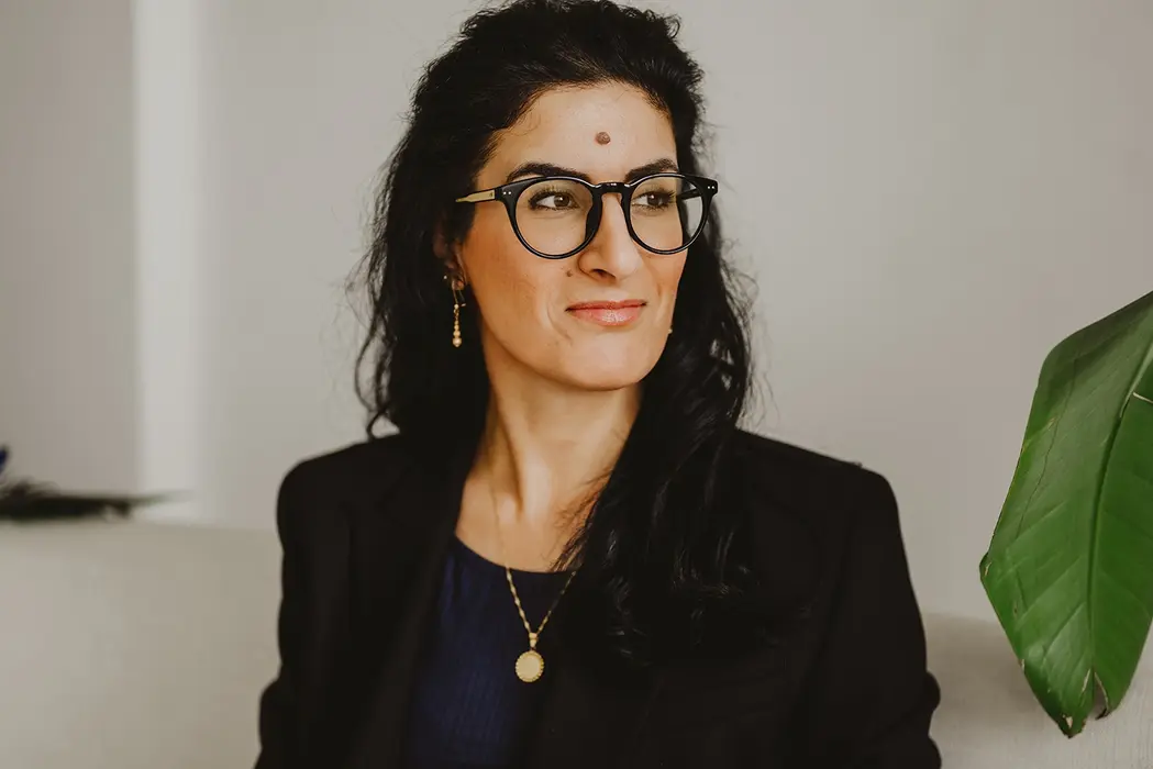 Nahaufnahme einer Frau mit Brille und dunklem Blazer neben grüner Pflanze – selbstbewusst, stilvoll und authentisch.
