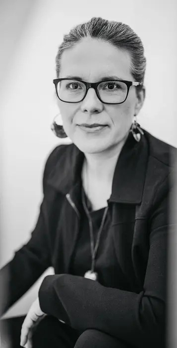 Schwarz-weiß Businessporträt einer Frau mit Brille und Blazer, sitzend und direkt in die Kamera blickend – professionelle und authentische Markenfotografie.