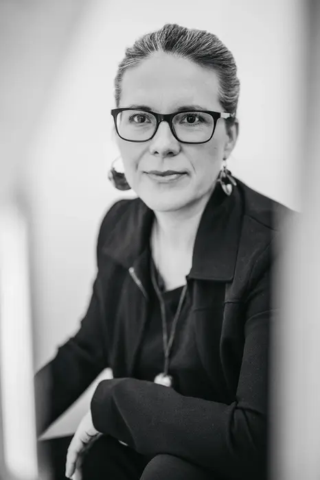Schwarz-weiß Portrait einer Frau mit Brille und markantem Schmuck in ruhiger Pose.