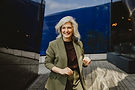 Selbstbewusste Businessfrau mit silberblonden Haaren in olivgrünem Hosenanzug, lachend in moderner urbaner Umgebung. Authentisches Personal-Branding-Foto mit natürlicher Ausstrahlung, das Professionalität, Nahbarkeit und Selbstvertrauen vermittelt.