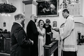 Heilige Momente mit einem Hauch von Humor: In der kirchlichen Trauung stehen das Brautpaar und ihre Trauzeugen gespannt für die Segnung bereit. Plötzlich wird die feierliche Stimmung von einem amüsanten Zwischenfall unterbrochen: Der Bräutigam lässt den Ring fallen, und die Braut kann ein herzhaftes Lachen nicht unterdrücken. Ein unvergesslicher Augenblick, der die heilige Zeremonie mit einer Prise Humor und der Leichtigkeit der Liebe durchzieht.